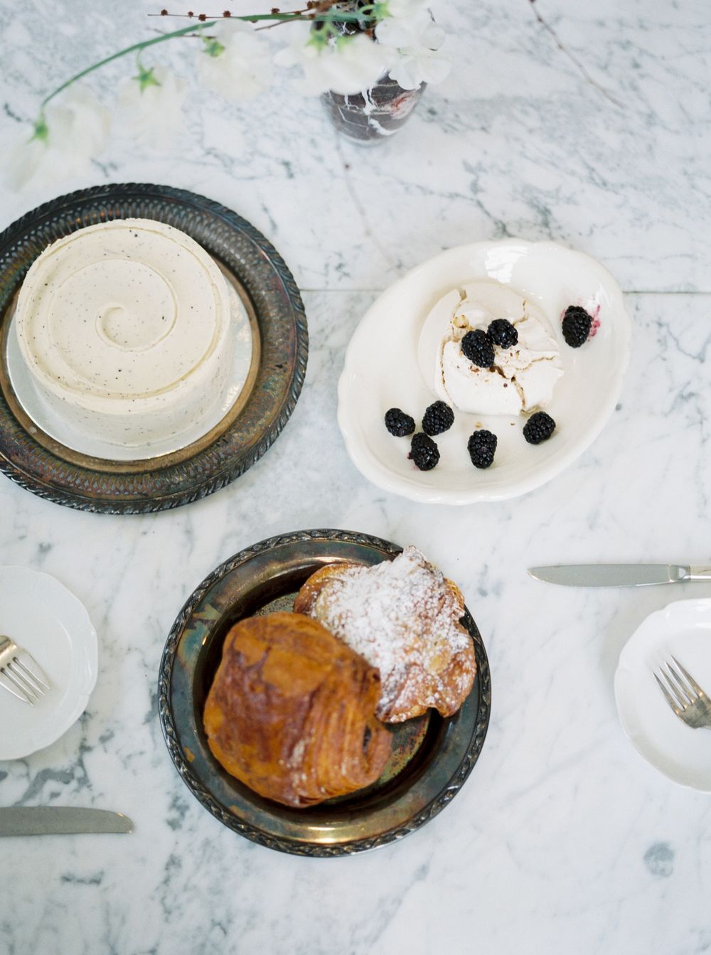 Breakfast spread on marble table with pastries, berries, and cream served on dark plates.