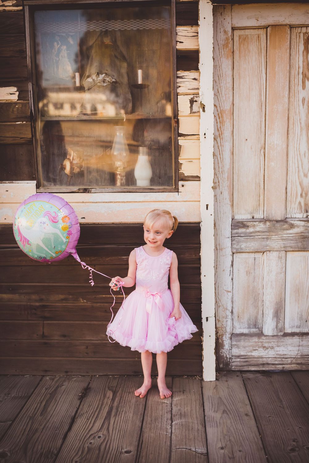A child in a pink dress plays with a colorful balloon on a rustic wooden porch in Beaumont, Ca.