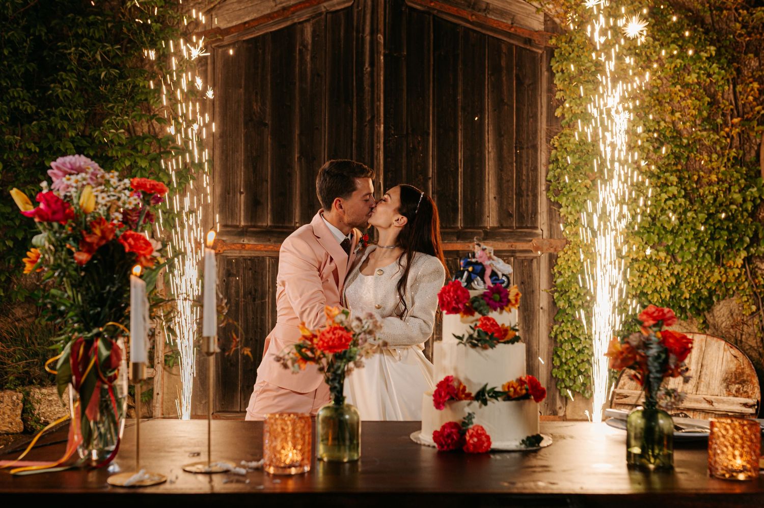 A romantic wedding reception scene with rustic wooden decor, glowing candles, and vibrant red floral arrangements.