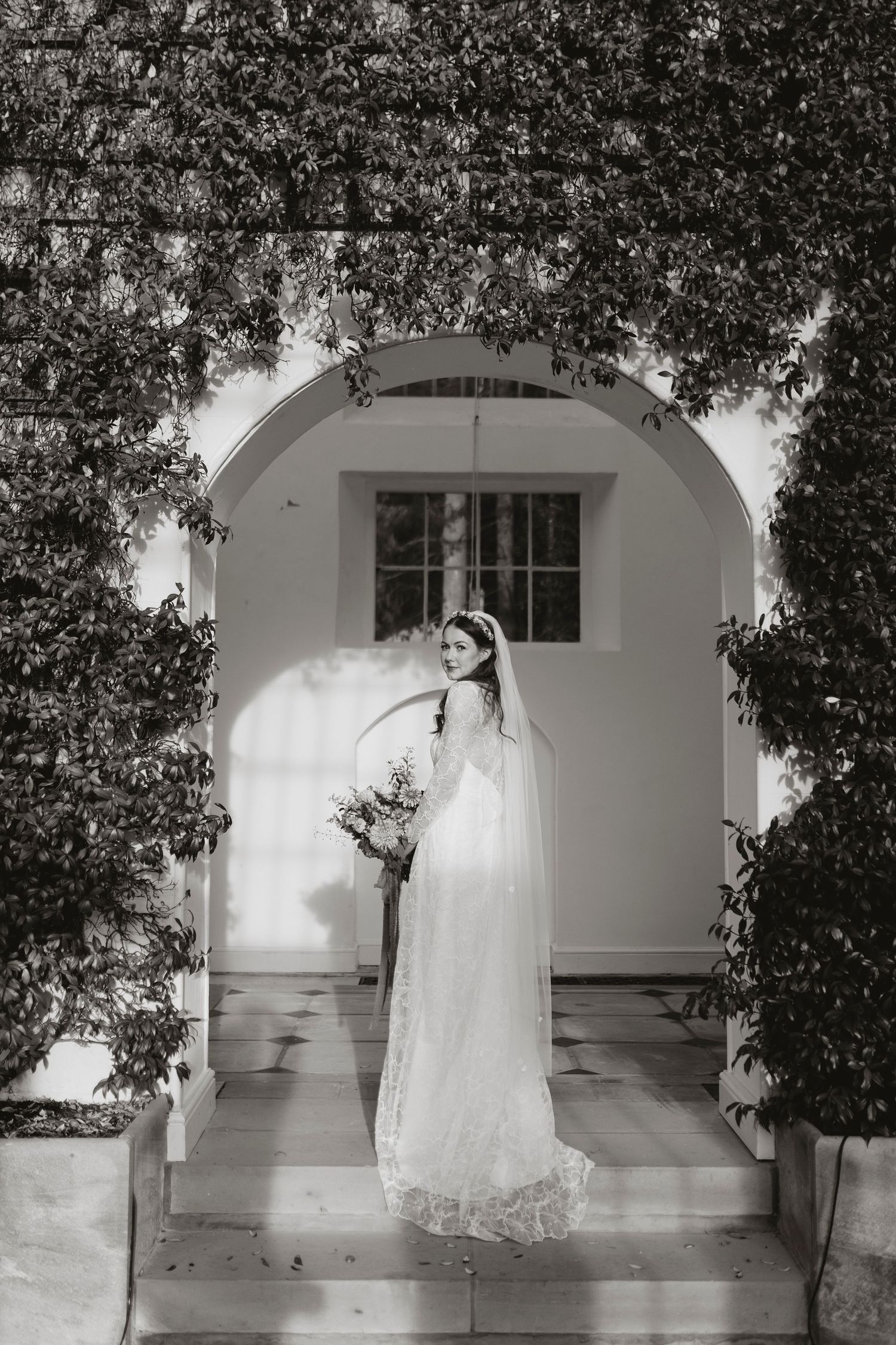 A bride in a flowing white wedding dress posing gracefully against a light archway at Hopton Court