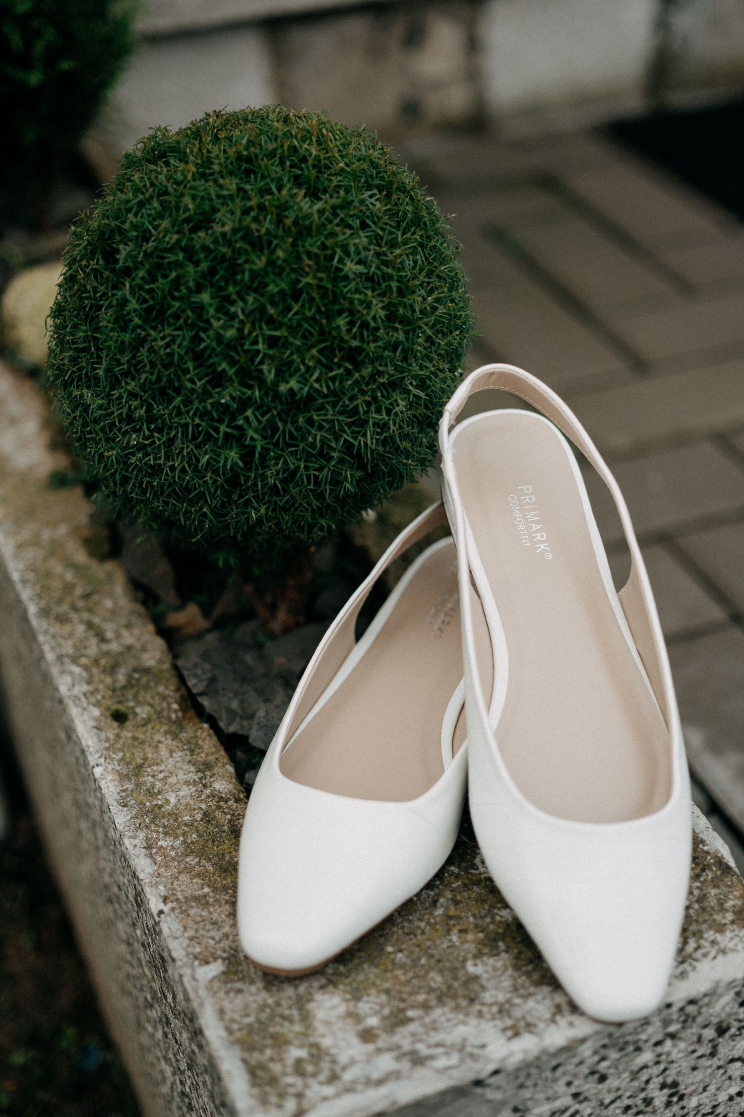White bridal flats displayed on a stone ledge next to decorative greenery.