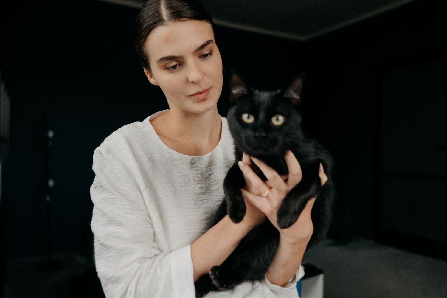 Person in white sweater holding black cat in dimly lit room.
