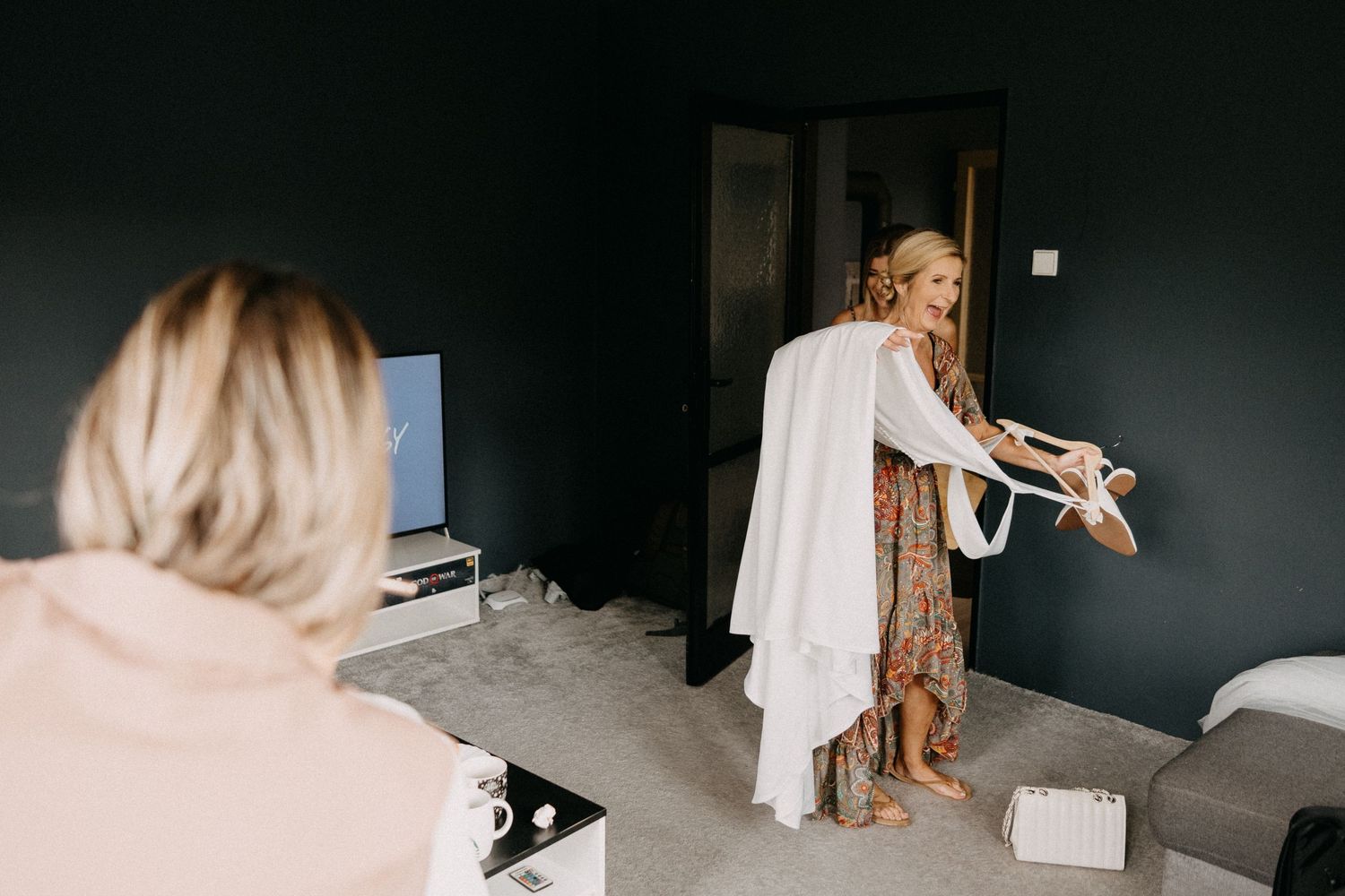 Two people in a room with dark walls, with one person wearing a white robe while standing near a couch.