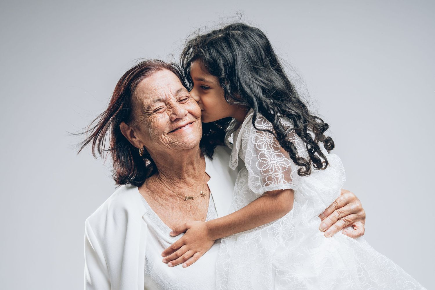 Two people share an intimate embrace and joyful moment against a light gray studio background.