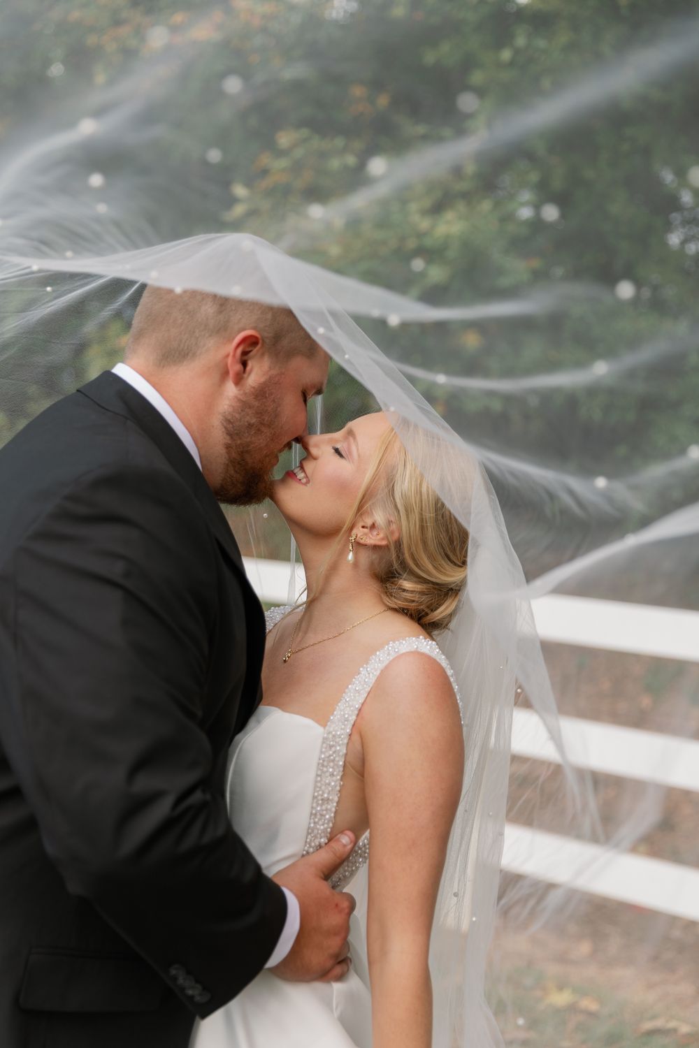 Romantic wedding couple shares an intimate moment under flowing veil during outdoor autumn photoshoot.