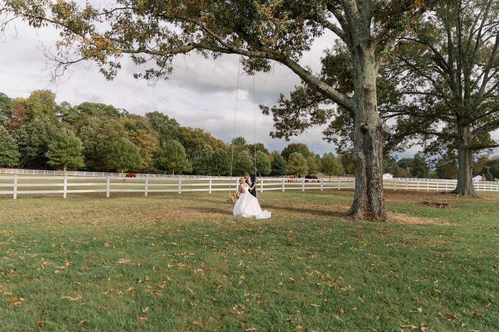 A bride in a white wedding dress walks through a scenic grassy field surrounded by autumn trees.
