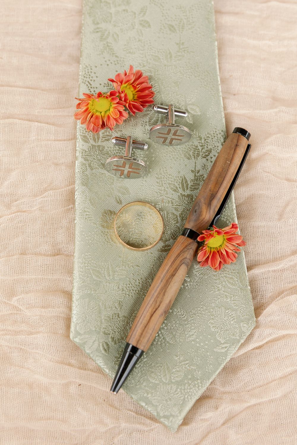 Wooden pens and orange gerbera daisies arranged on mint green fabric with delicate floral patterns.