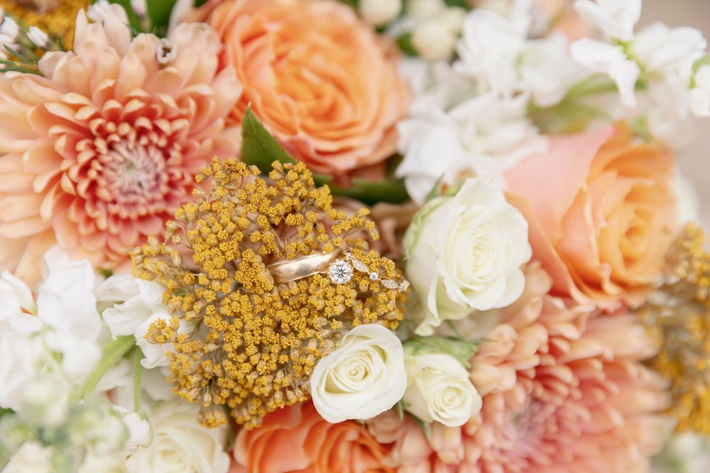 Wedding rings nestled among peach roses, white flowers and golden yarrow in an elegant bridal bouquet.
