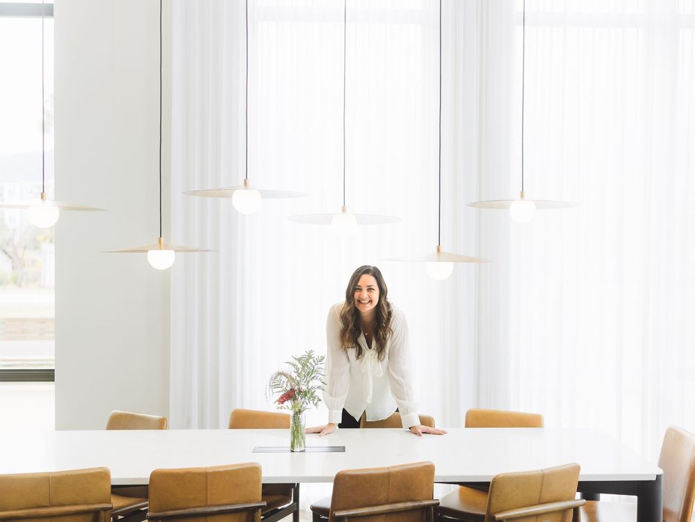 A bright, minimalist conference room with wooden chairs and pendant lights hanging from a white ceiling.