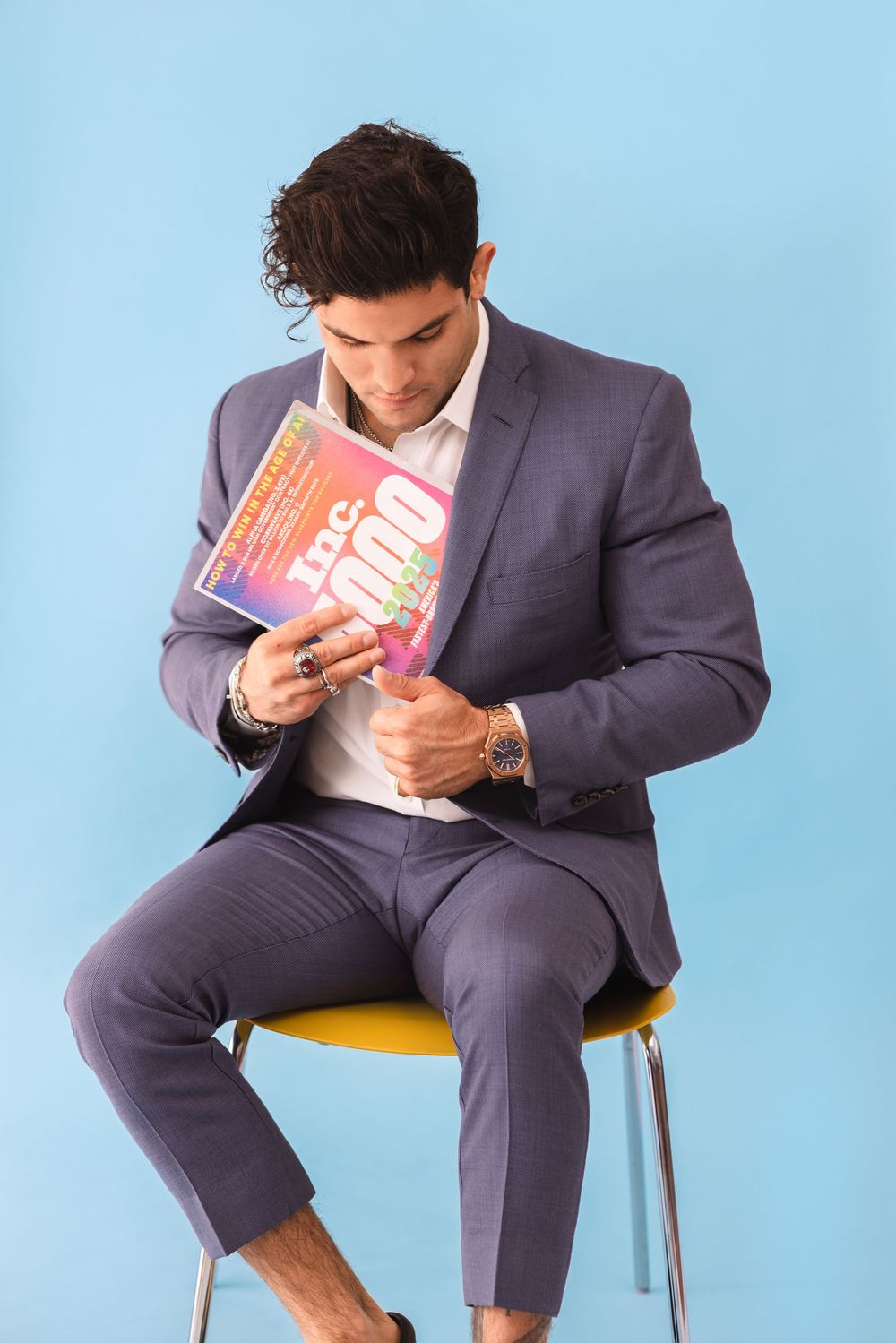 Person in grey suit sits reading a small pink book against light blue background.