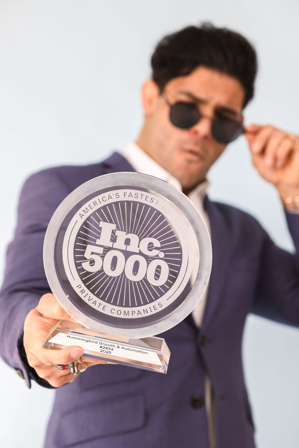Business person in suit holds Inc. 5000 company award plaques against white background.