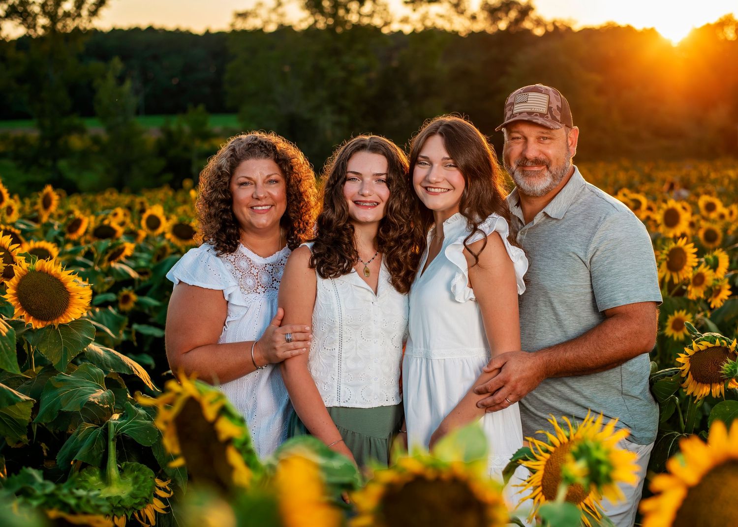 A group of people stand together in a golden sunflower field during sunset, creating a warm and joyful atmosphere.