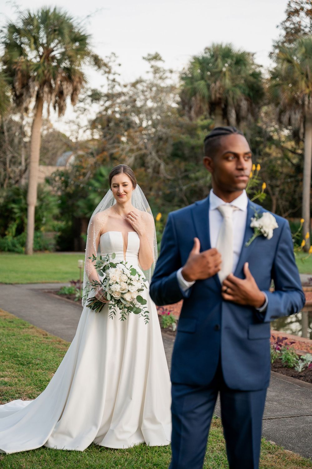 Wedding couple poses outdoors against a backdrop of palm trees and natural greenery.