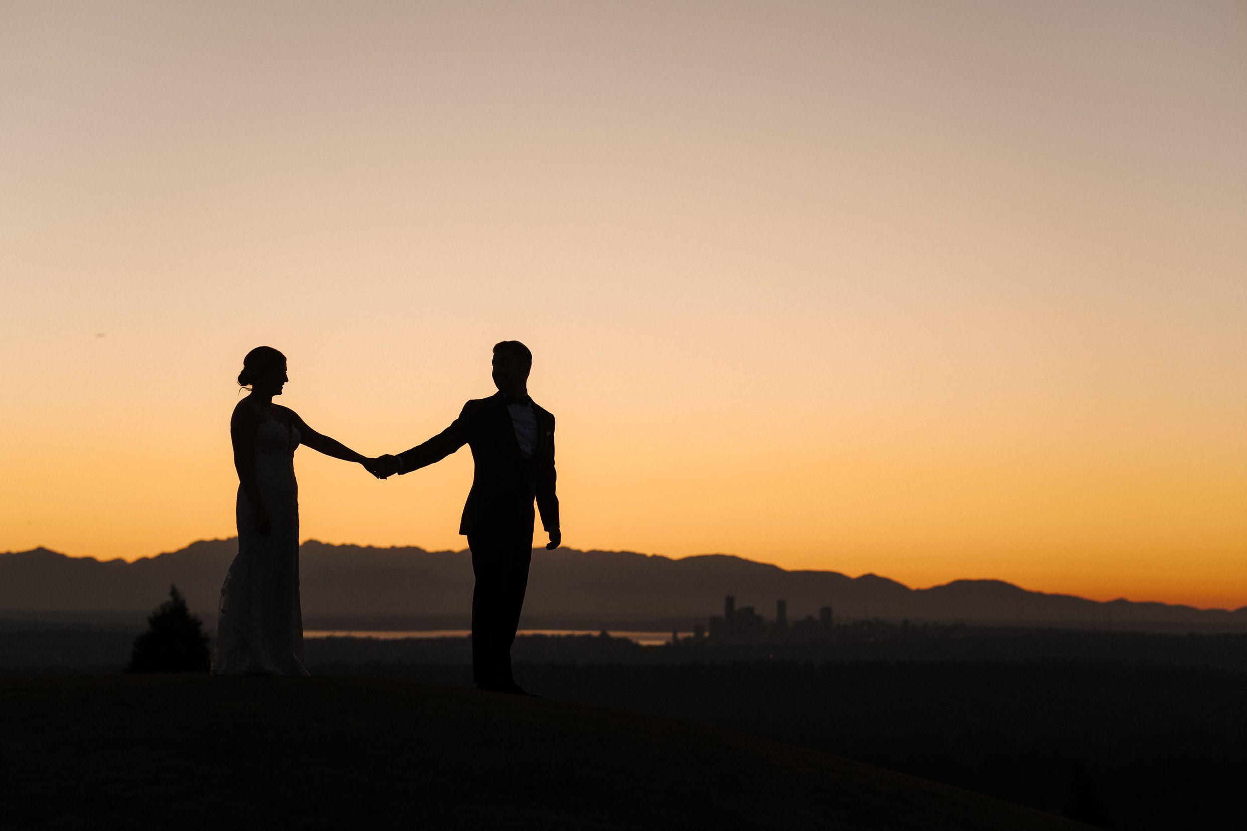 Silhouettes of two people standing on a hill against a vibrant orange sunset sky.