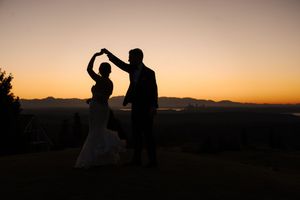 Silhouetted figures dance against a vibrant orange sunset sky with mountains in the background.