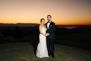 Romantic sunset silhouettes of a couple in wedding attire standing on a hilltop against an orange sky.