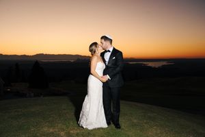 A couple in wedding attire shares a romantic moment at sunset against a scenic mountain backdrop.
