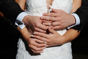 Close-up detail shots of hands with wedding rings against white bridal dress fabric.