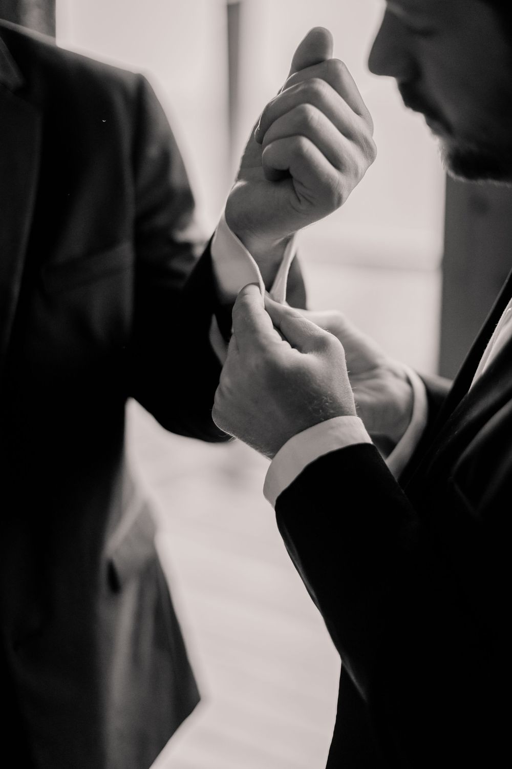 Close-up black and white shots of hands adjusting formal attire during a wedding preparation.