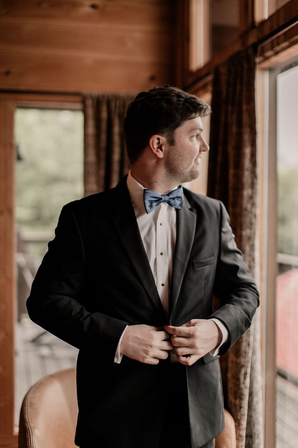 Groomsmen in formal attire and bow ties adjust their suits in a rustic wooden room.