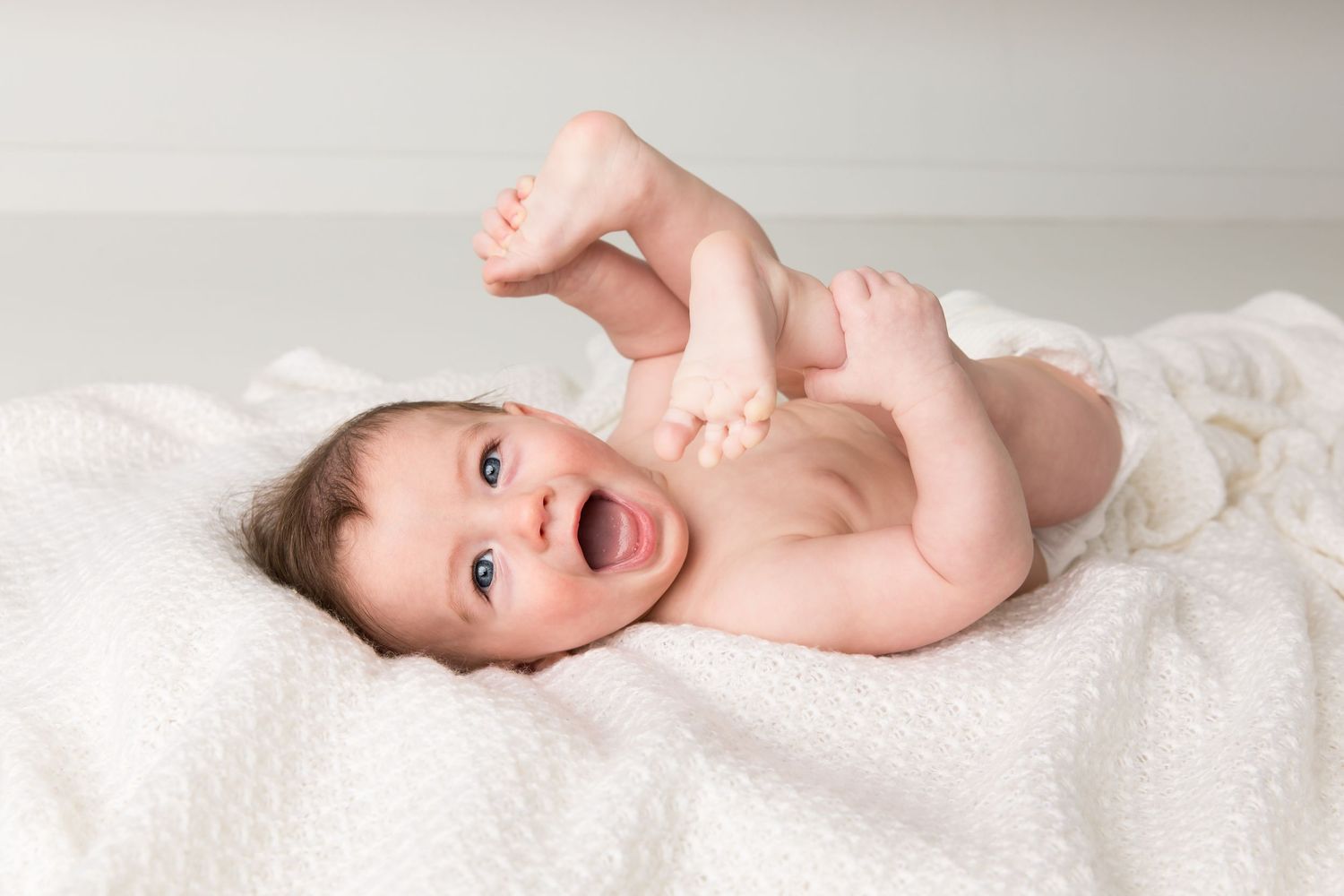 Baby lying on white blanket during newborn photography session.