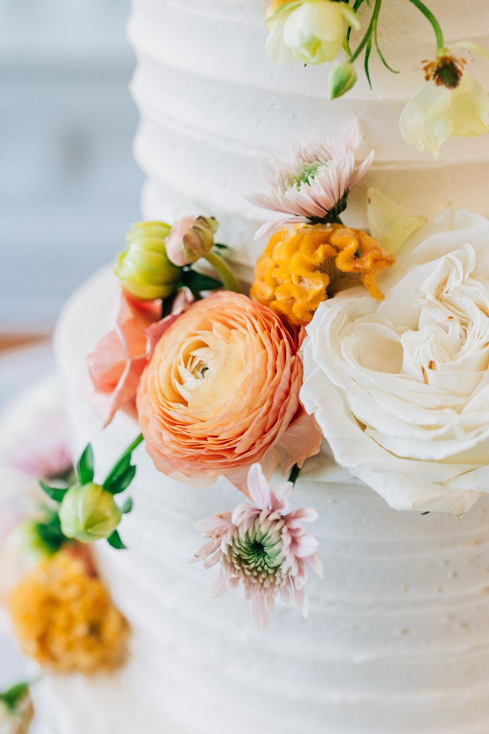 Close-up of a white wedding cake decorated with peach ranunculus, white roses and yellow flowers at 255 Milledge, Hardeman - Sams Estate