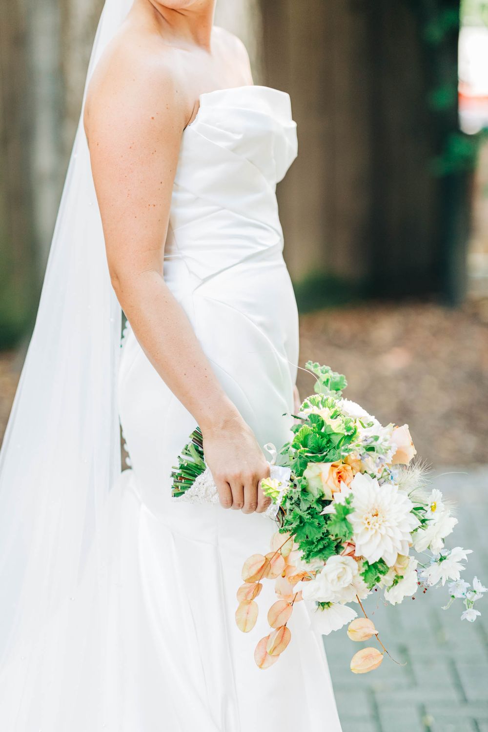A bride in a white wedding dress holds a beautiful bouquet of peach and white flowers with greenery at 255 Milledge, Hardeman - Sams Estate