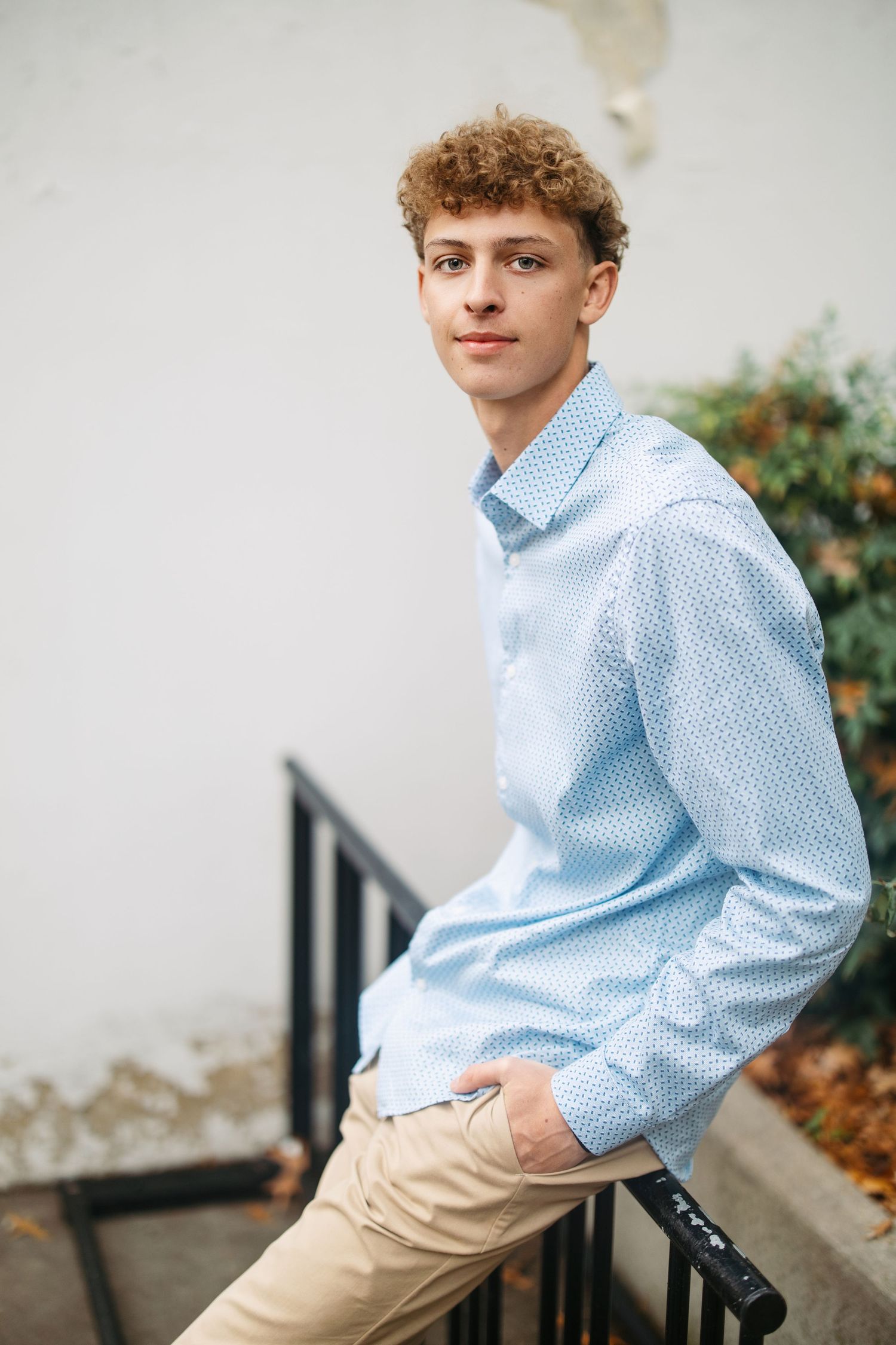 Young person in light blue button-down shirt and khaki pants poses casually on outdoor steps.