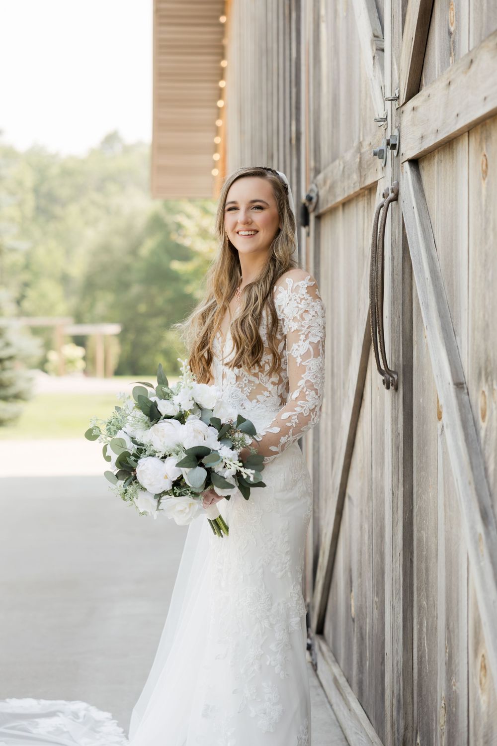 Bride in long sleeve lace wedding dress poses in front of rustic barn door.