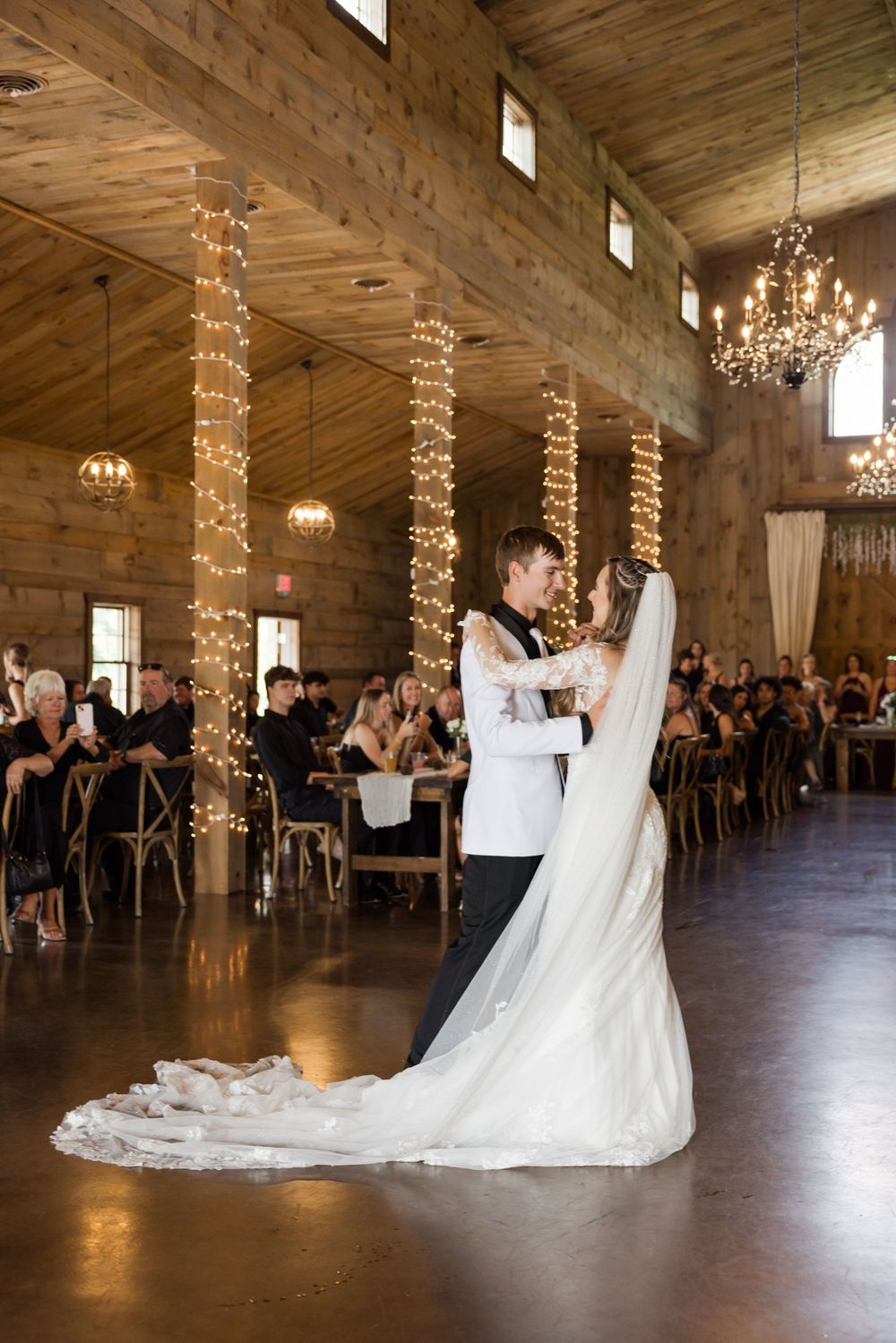 Elegant wedding ceremony in rustic barn venue with twinkling string lights and wooden beams.