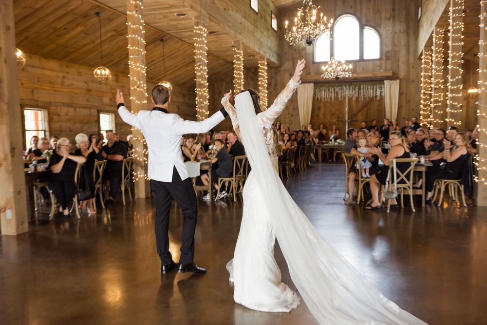 Wedding reception dance in rustic barn venue with string lights and wooden beams.