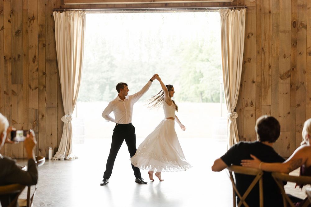 Dancing and celebration in a sunlit rustic barn venue with flowing white curtains.