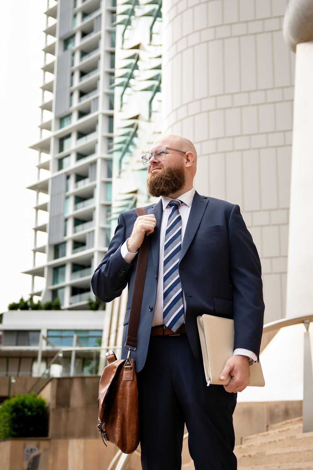 Business professional in a navy striped suit stands outside a modern office building with white columns.