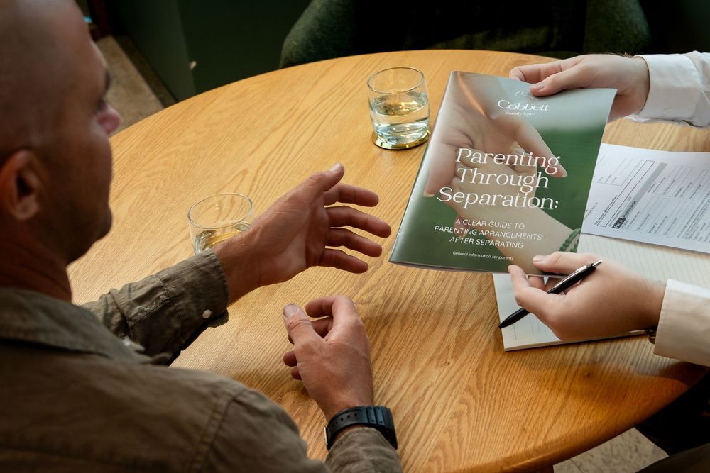 Hands holding a pen and writing notes on paper at a wooden desk during a meeting or study session.