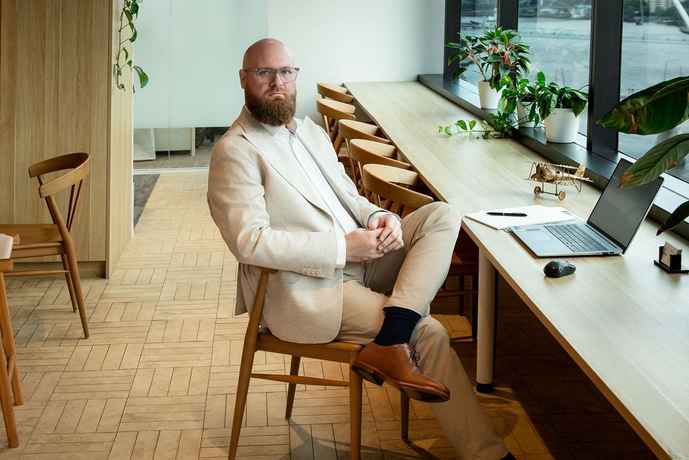 Professional in white blazer working at modern minimalist desk with laptop and plants in bright office space.