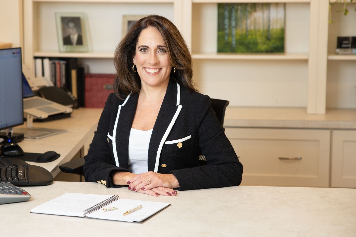 Professional in business attire smiles while sitting at desk in office setting.