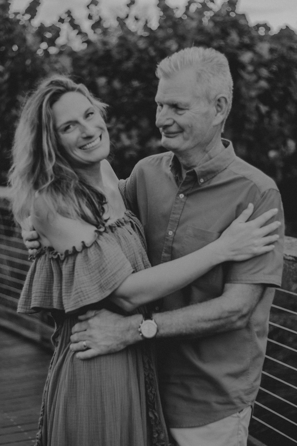 A couple embraces and laughs together while sitting on a park bench in black and white.