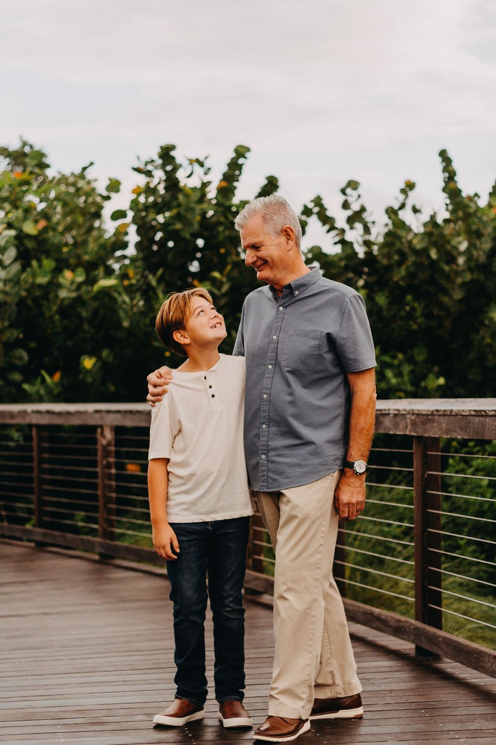 Two people share a joyful moment together while standing on a wooden boardwalk surrounded by greenery.
