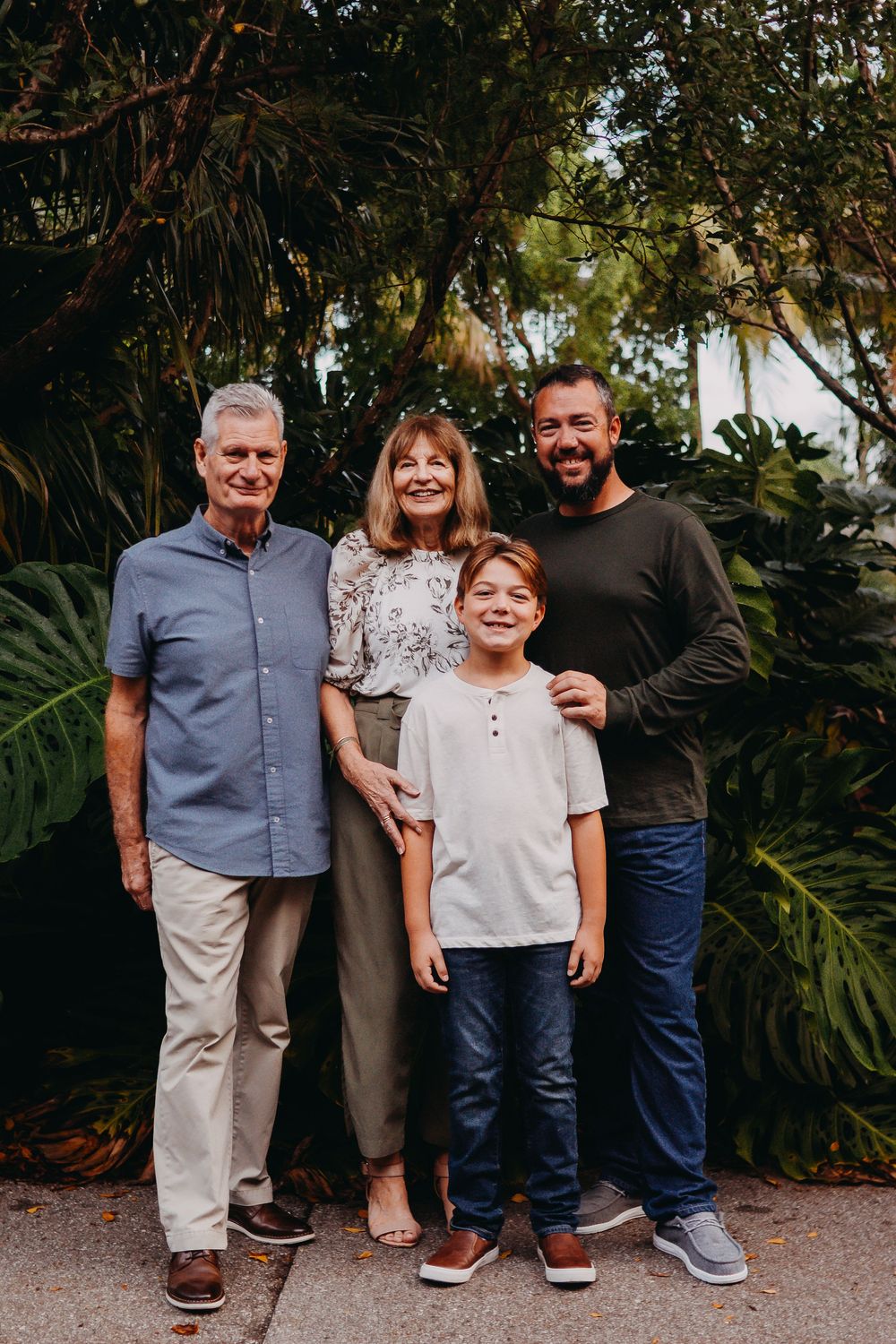 A family poses together in front of lush tropical foliage at a garden or park setting.