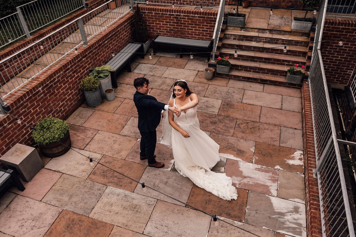 A couple in wedding attire walks up brick stairs while guests look on during an outdoor ceremony.