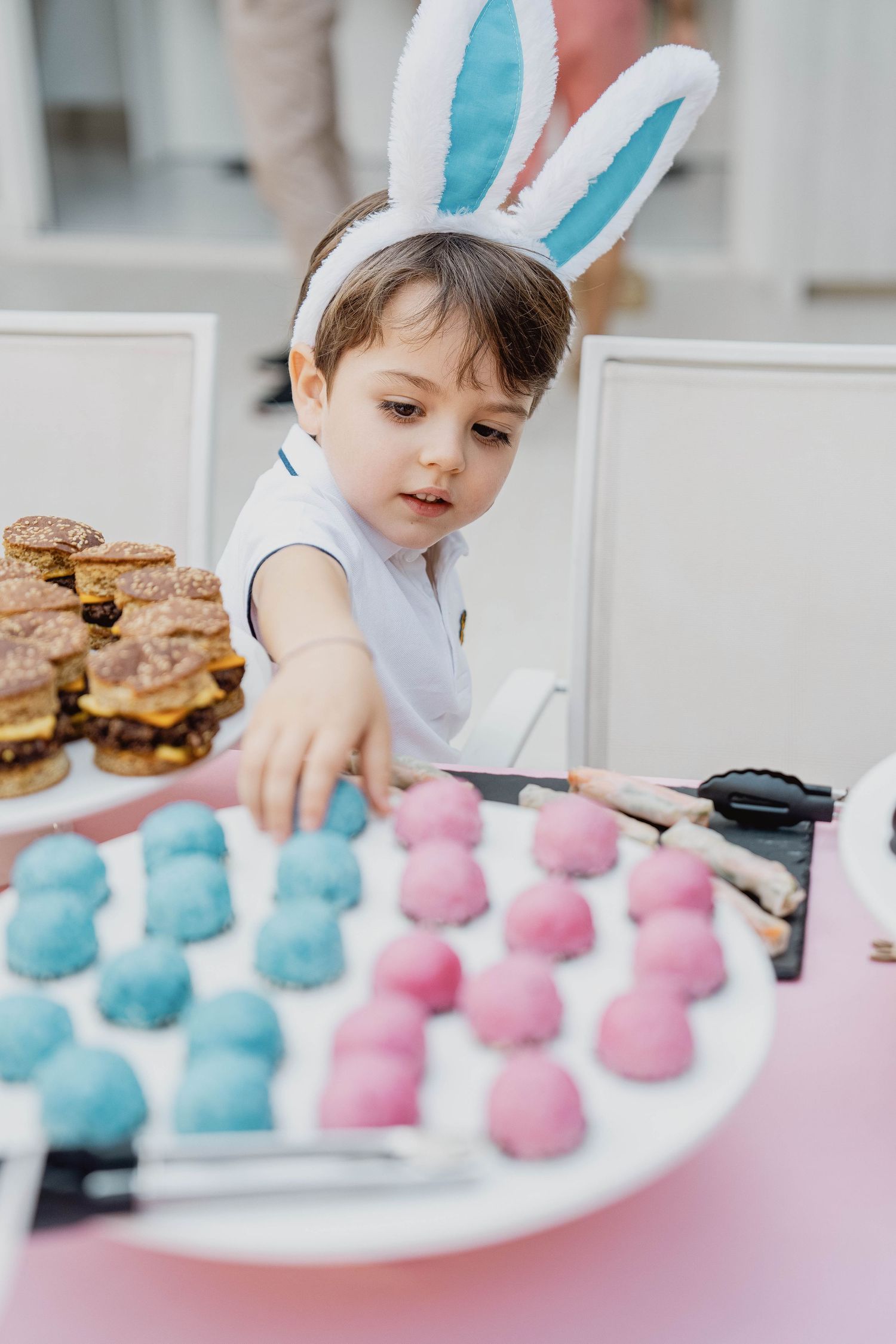 Toddler wearing bunny ears sitting beside pastel party treats