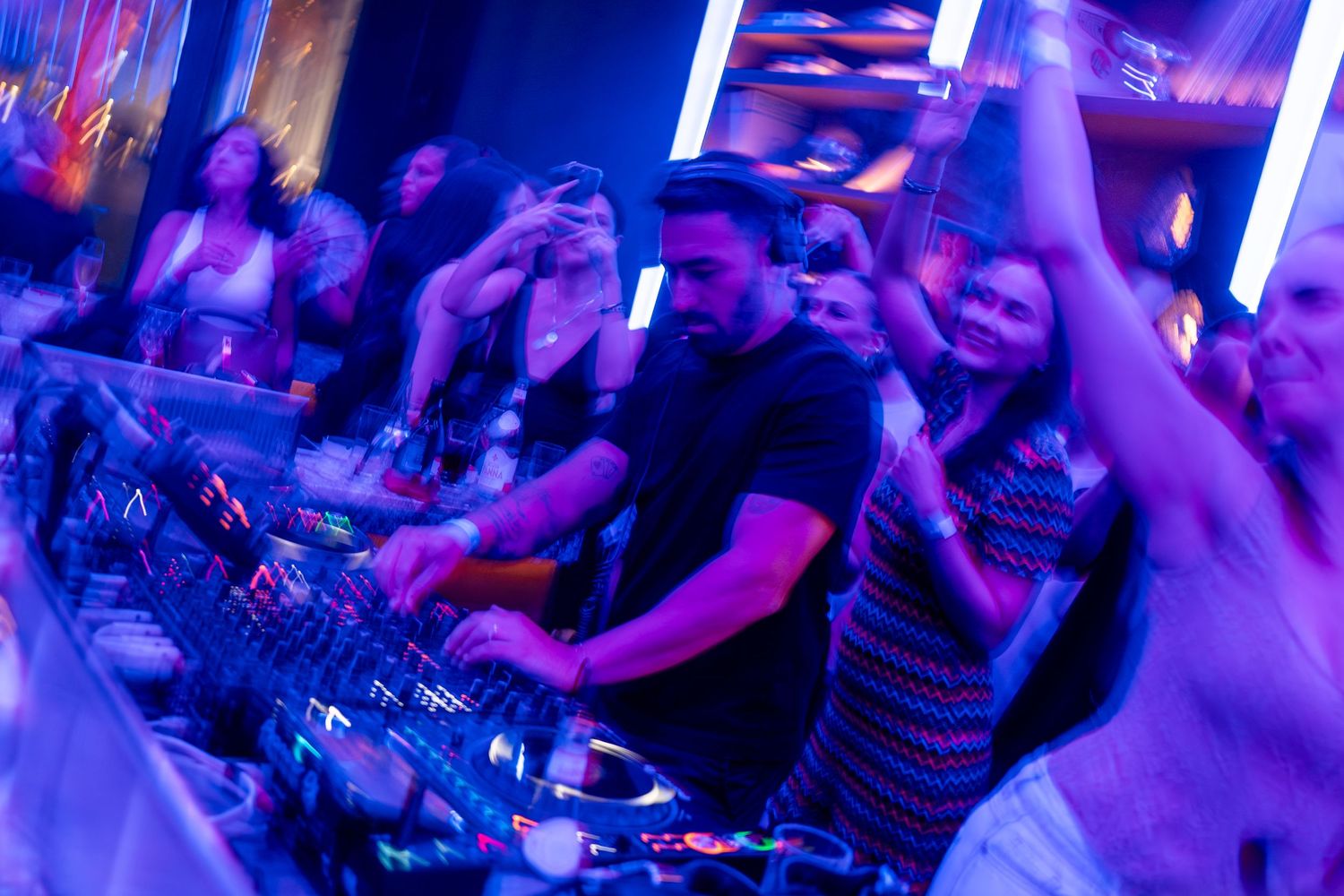 Party guests cheering around DJ booth under neon lighting