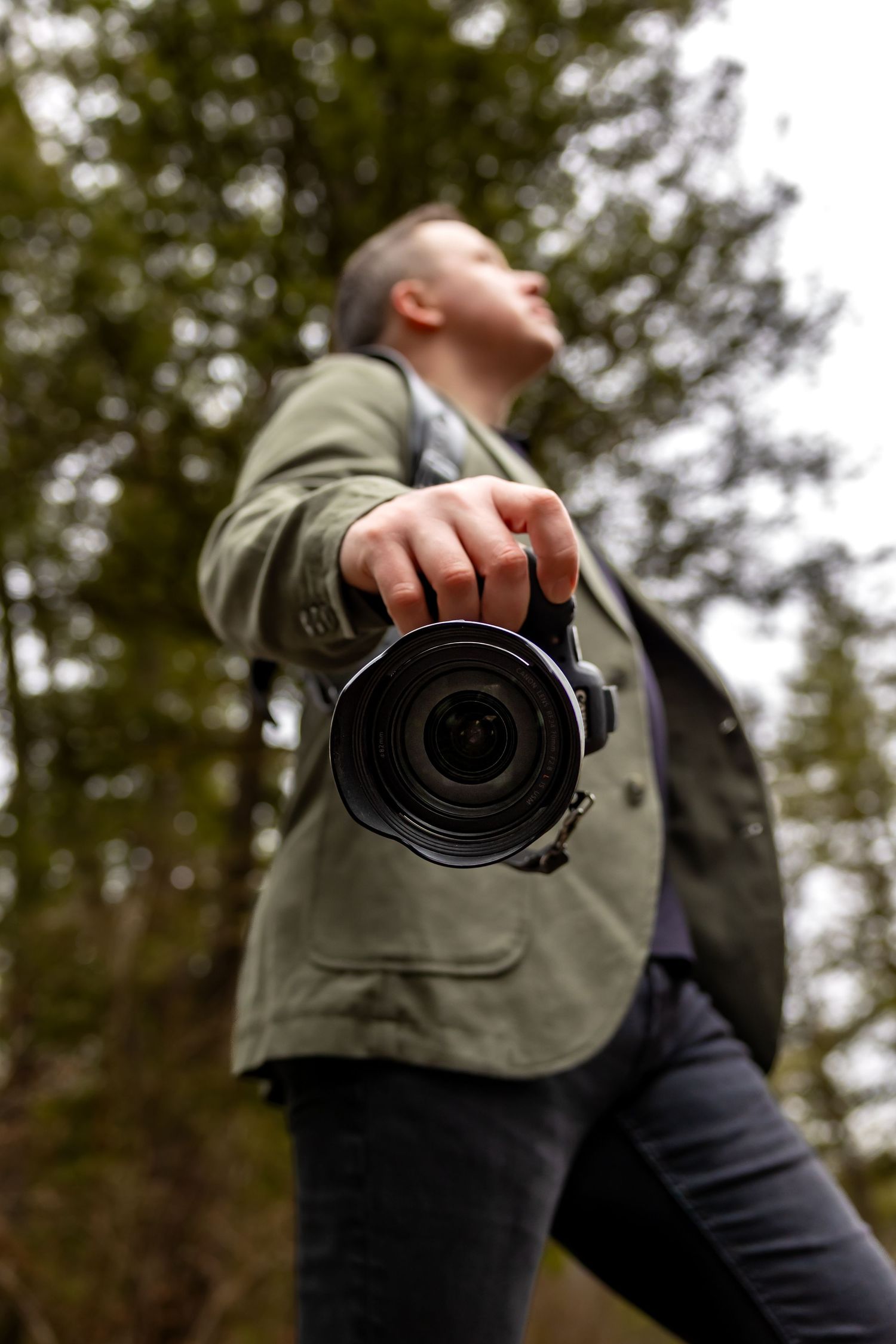 A photographer in an olive jacket holds a camera at different angles against a blurred forest background.