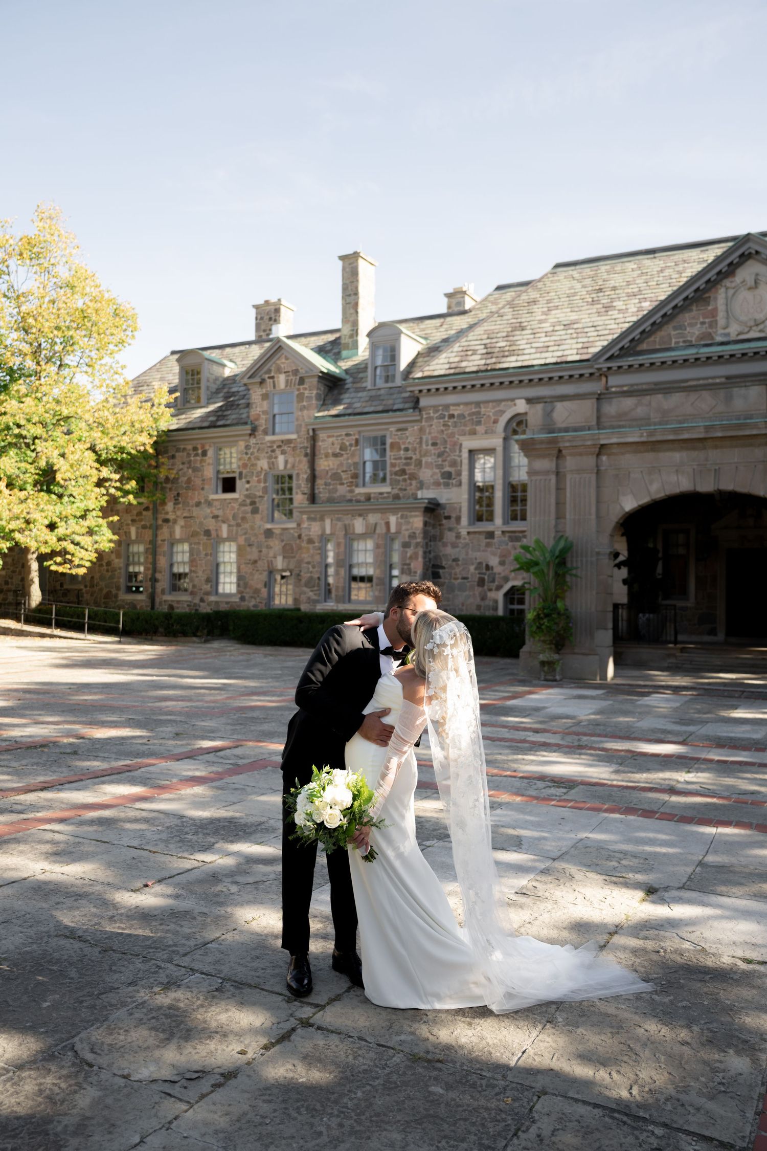 A wedding couple stands outside of Graydon Hall Manor Toronto with arched entrance and ornate architectural details.