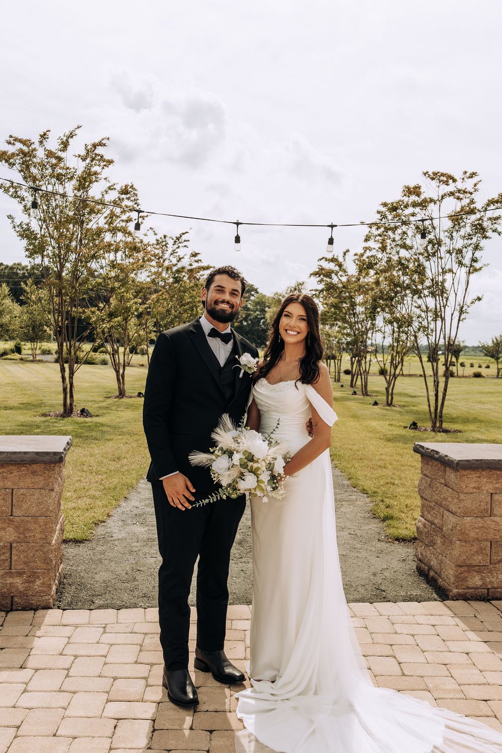 Bride and groom posing together on a brick patio surrounded by trees at their wedding venue.
