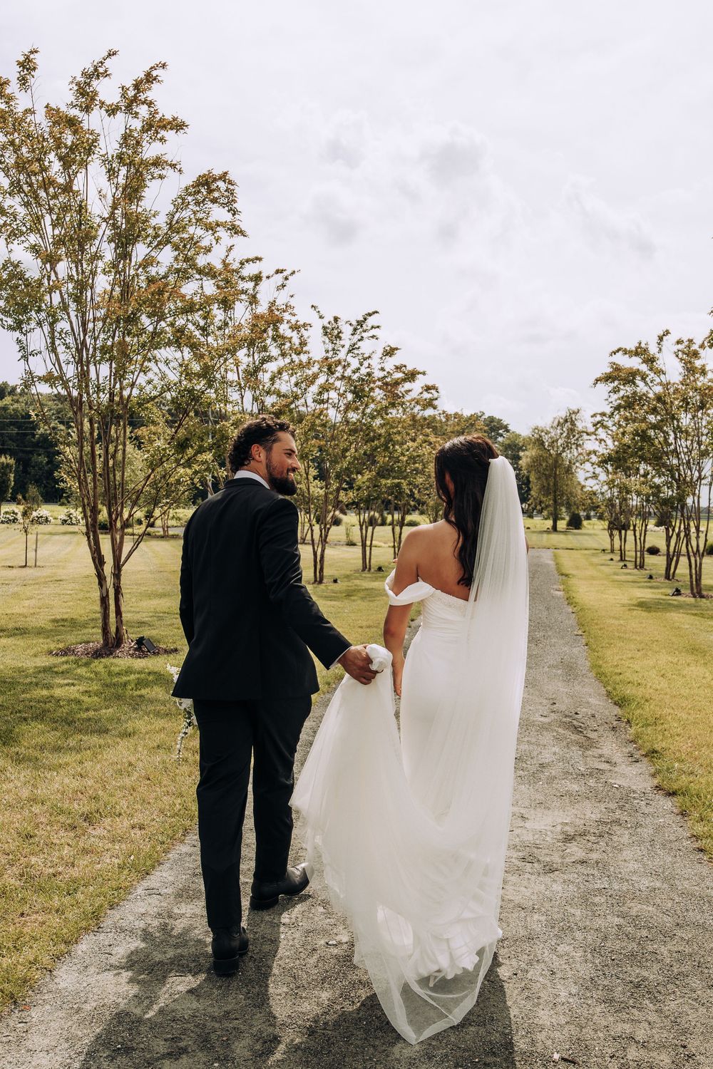 Bride and groom walking hand in hand down a tree-lined path at their outdoor wedding.