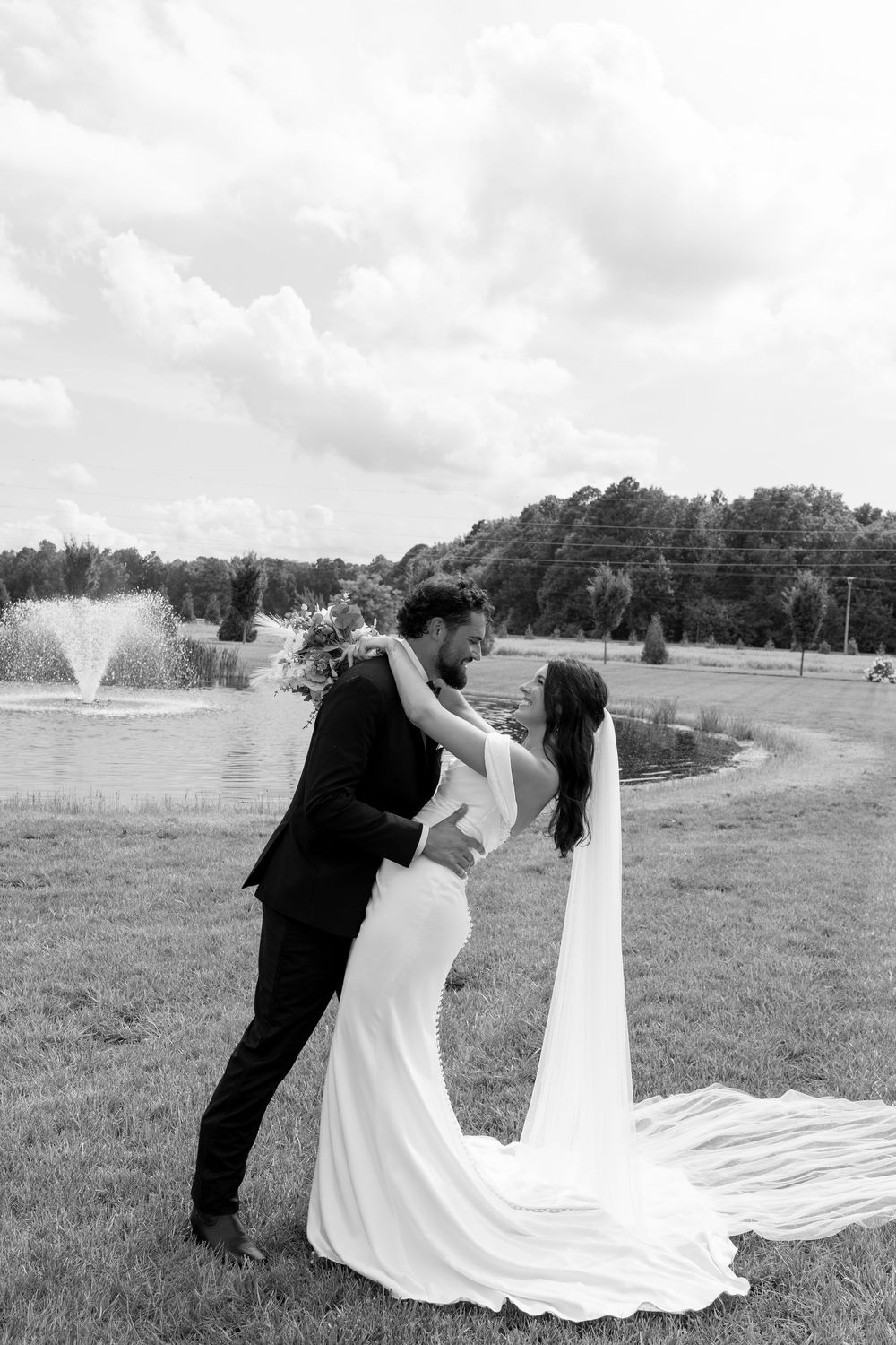 Black and white photo of bride and groom sharing romantic moment by pond on wedding day.