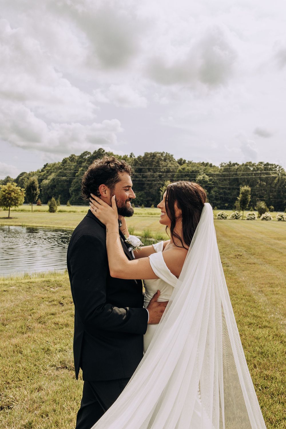 Bride and groom gaze lovingly at each other near scenic pond on their wedding day.