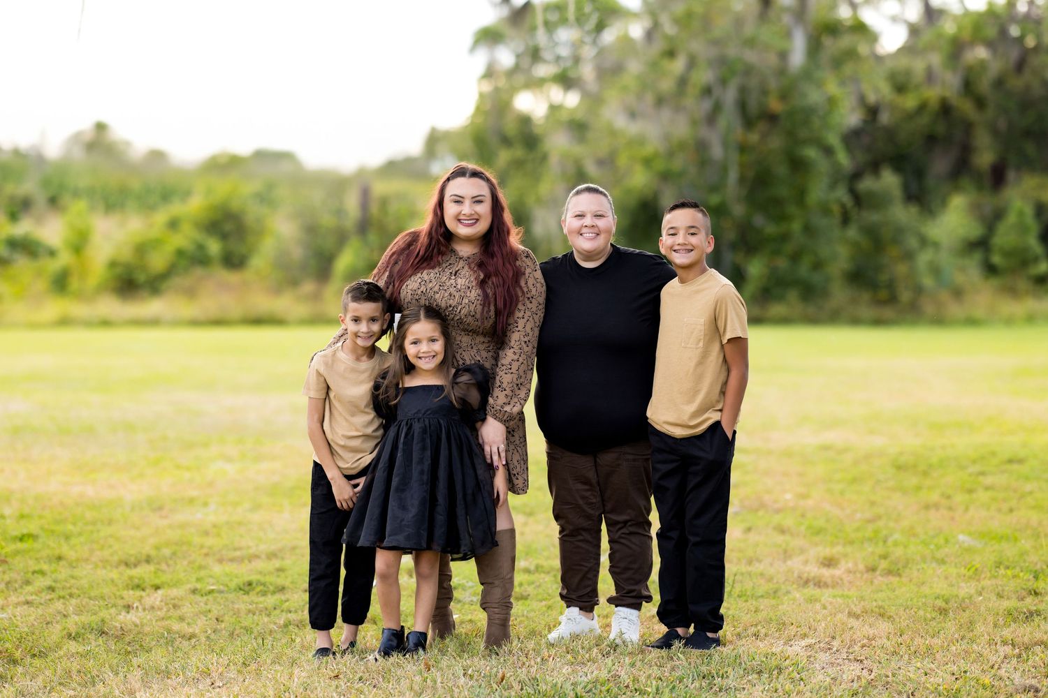 A series of candid outdoor family portraits showing people walking and posing together in a grassy field on a sunny day.
