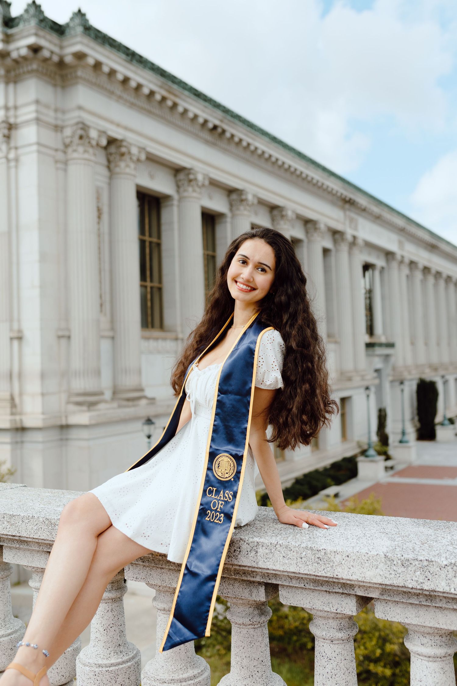 UC Berkeley graduate poses outside one of the campus's beautiful buildings (Doe Library) for her grad photoshoot. She wears her grad sash.